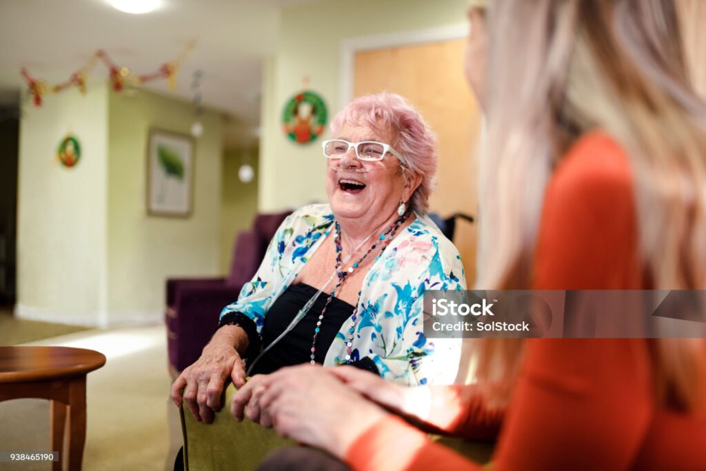Senior woman talking to a younger woman who is visiting her while she is living in the care home. The senior woman has pink hair